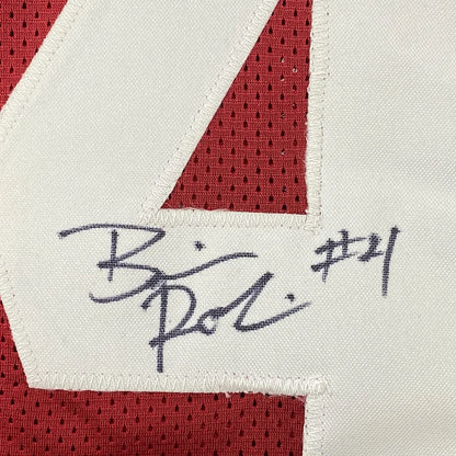 A red and white Alabama football jersey with number 21 and Brian Robinson Jr signed in black ink on fabric