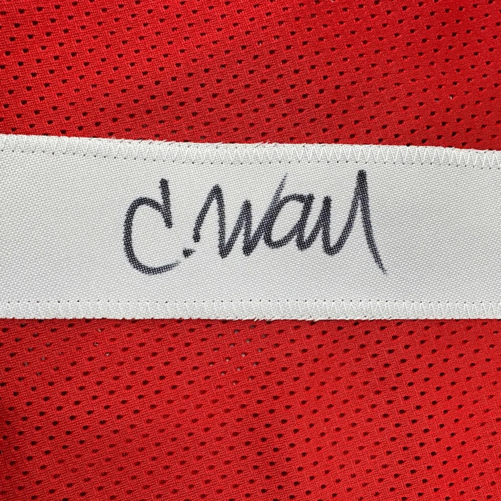 A white woven label with a black cursive signature on a framed autographed san francisco 49ers red football jersey
