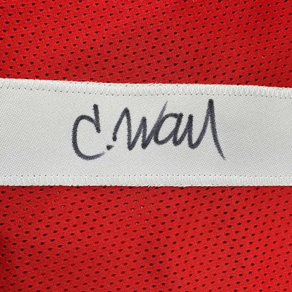 A white woven label with a black cursive signature on a framed autographed san francisco 49ers red football jersey