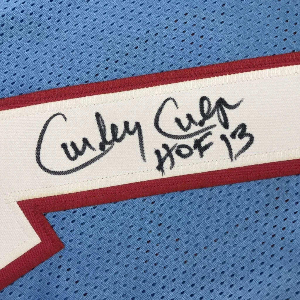 A white label with black ink signature and hof 13 text bordered in red stitched on light blue mesh Houston football jersey