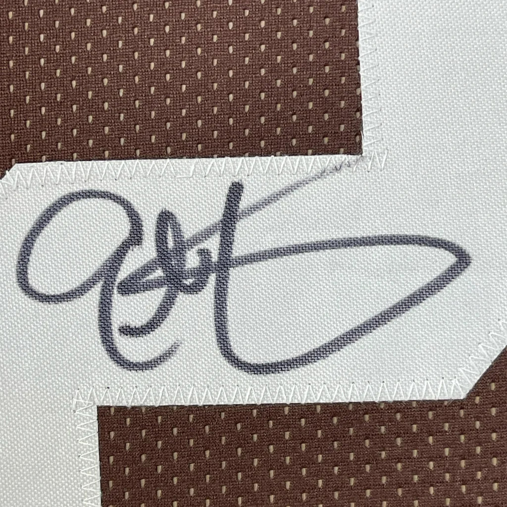 Black embroidered signature on white fabric patch stitched on brown mesh of framed signed eric metcalf cleveland brown jersey