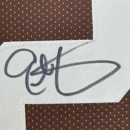 Black embroidered signature on white fabric patch stitched on brown mesh of framed signed eric metcalf cleveland brown jersey