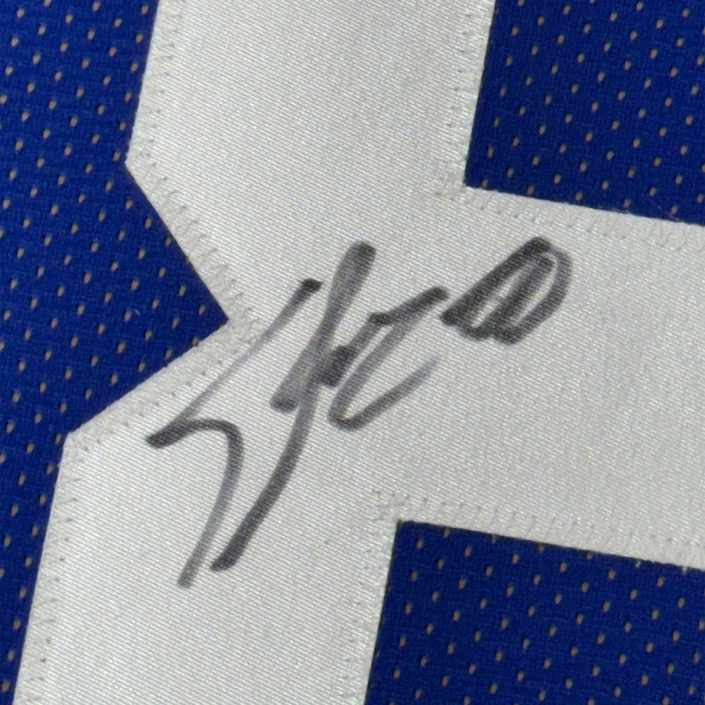 A close-up of Jeremy Shockey signature in black ink on the white fabric panel of a blue and white football jersey