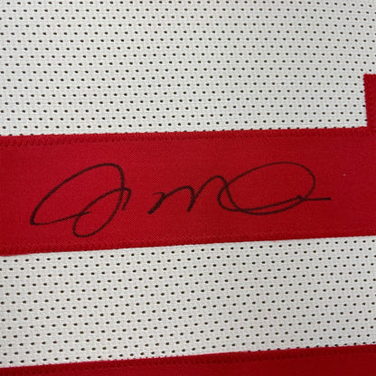 White athletic jersey with red stripe and black signature, perfect for display