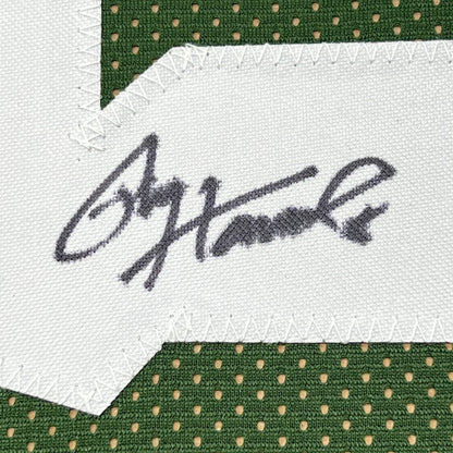 A black ink ogorman signature stitched on white fabric patch bordered by green mesh on a framed signed green bay jersey