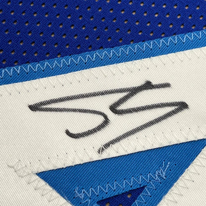 A white fabric patch with a black embroidered Shaquille O’Neal signature on a blue mesh framed basketball jersey