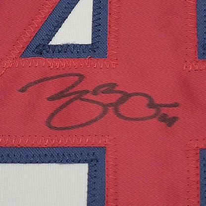 Red sports jersey with white and blue stitched numbers and black autograph, professionally framed