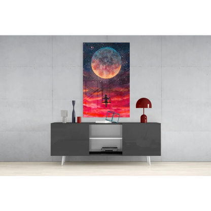 Vibrant glass wall art of glowing orange blue moon, starry sky, pink clouds, silhouette on swing
