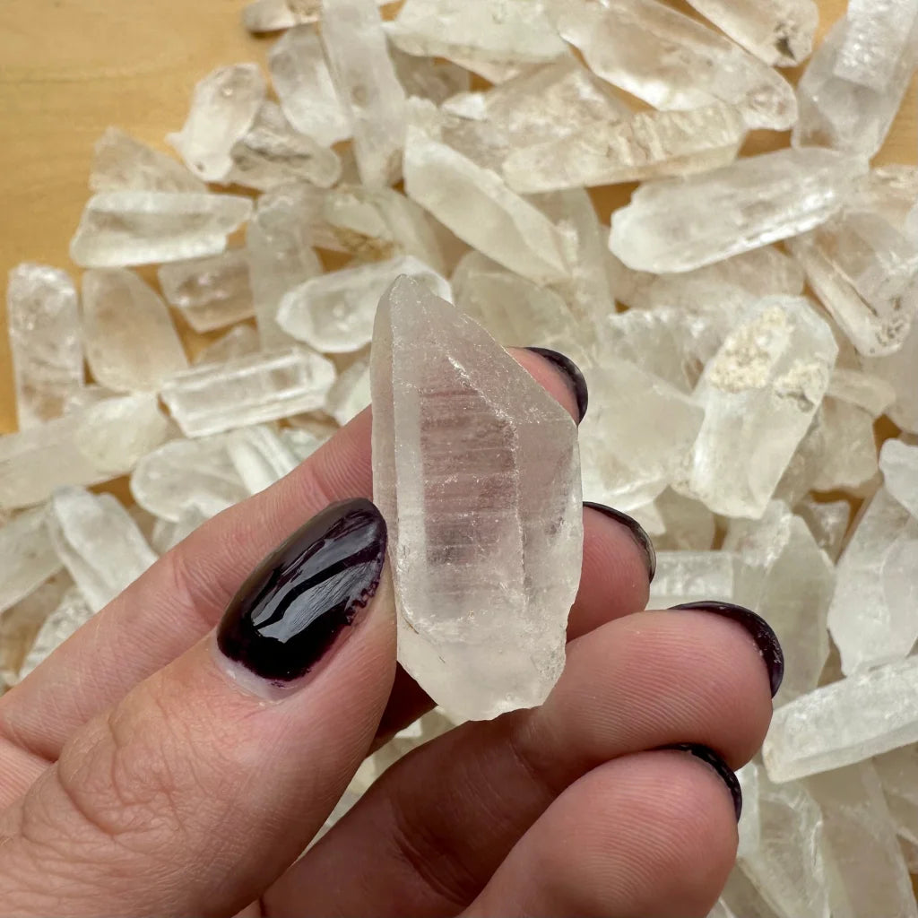 Hand holding translucent Brazilian quartz crystal with dark nails