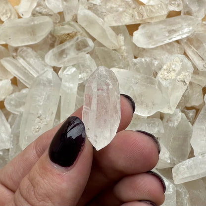 Clear faceted Brazilian quartz crystal point held by fingers with dark nails