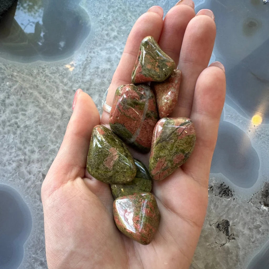 Hand holding large tumbled jasper stones in green and pink hues for crafts