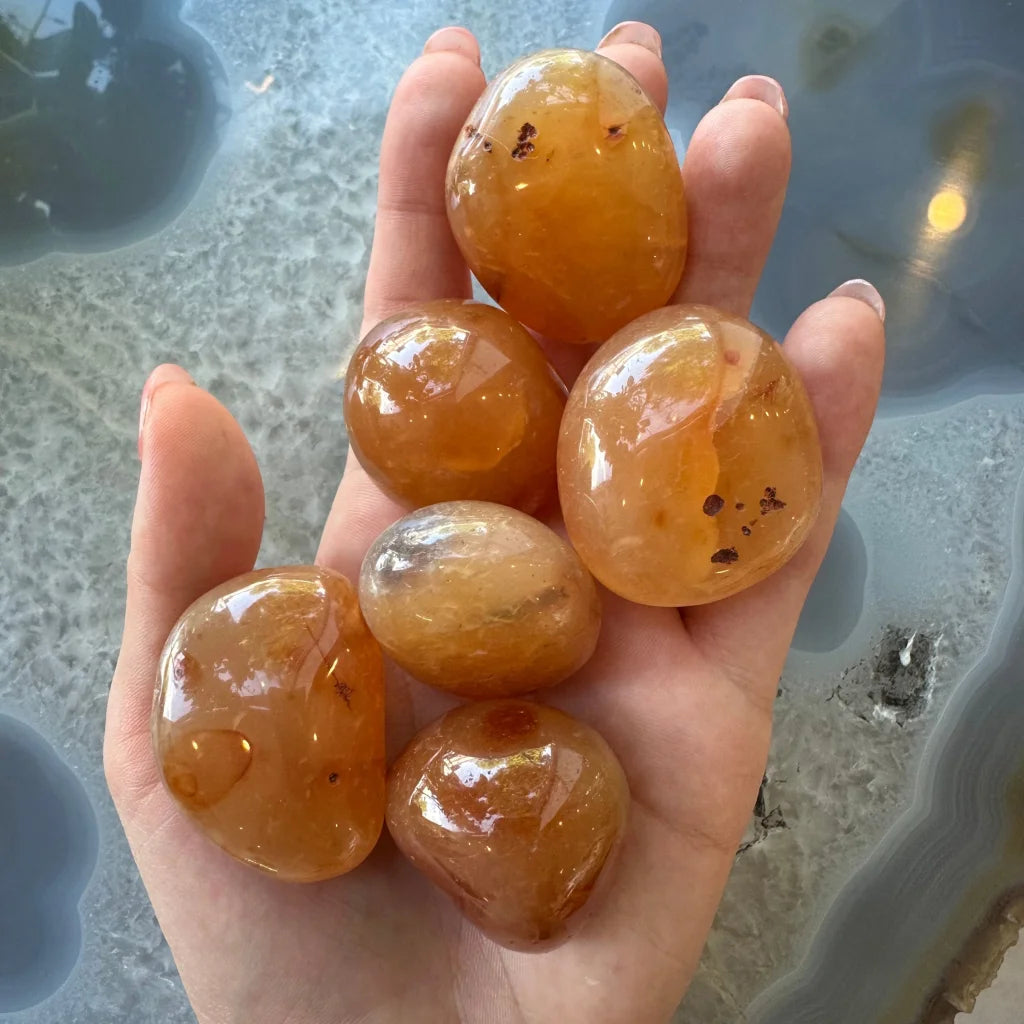 Hand holding six large tumbled stones in amber tones for crafts