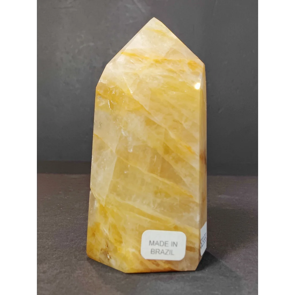 A polished yellow-orange golden healer quartz obelisk tower sculpture with natural striations and made in Brazil label