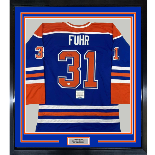 Framed Edmonton Oilers blue hockey jersey number 31 with "FUHR" nameplate and authenticity certificate displayed behind glass with orange and blue matting.