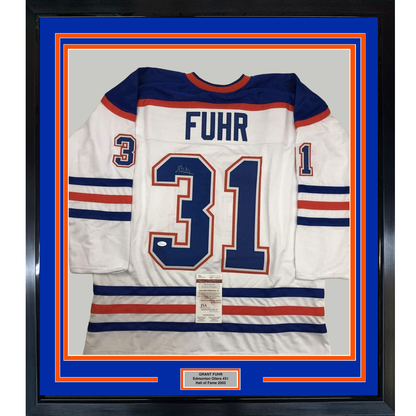 Framed white Edmonton Oilers hockey jersey number 31 with "FUHR" nameplate and JSA authentication certificate, displayed against blue and orange matting with black frame.