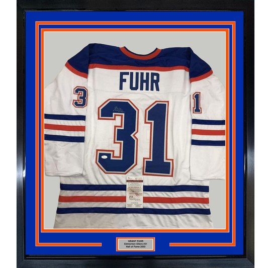 Framed white Edmonton Oilers hockey jersey number 31 with "FUHR" nameplate and JSA authentication certificate, displayed against blue and orange matting with black frame.