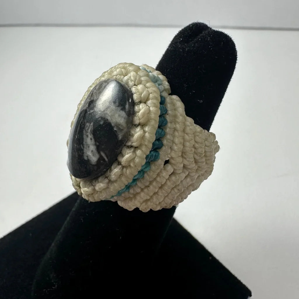 Cream-colored handmade woven ring with dark polished stone and teal accents
