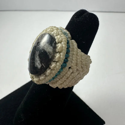 Cream-colored handmade woven ring with dark polished stone and teal accents