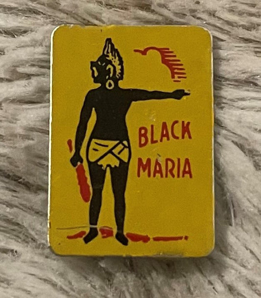 Front of the yellow Black Maria tobacco tag, printed figure and red lettering, on a gray textured surface.