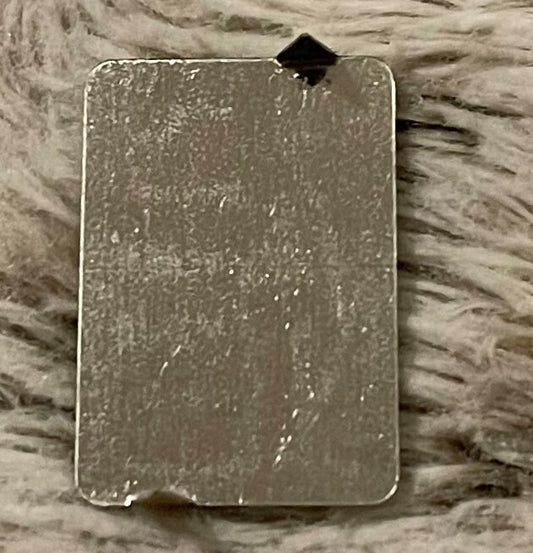 Reverse of the tag: worn silver-toned metal with a dark diamond-shaped prong at the top edge, on a gray faux-fur surface.