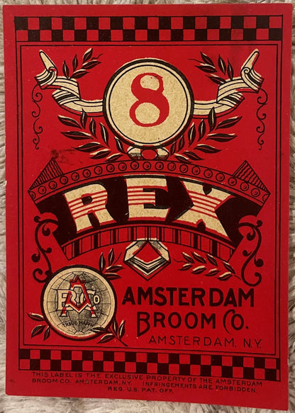 Vintage red chromolithograph broom label with gold circle containing number 8, decorative banners, laurel wreaths, and Amster