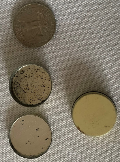 Four vintage tins and a coin for scale on white fabric, showing worn cream and speckled surfaces with embossed text on top ti