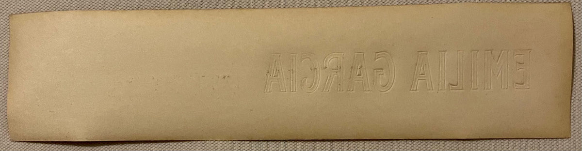 Embossed tan cigar box label with "EMILIA GARCIA" text visible, shown flat against textured fabric background