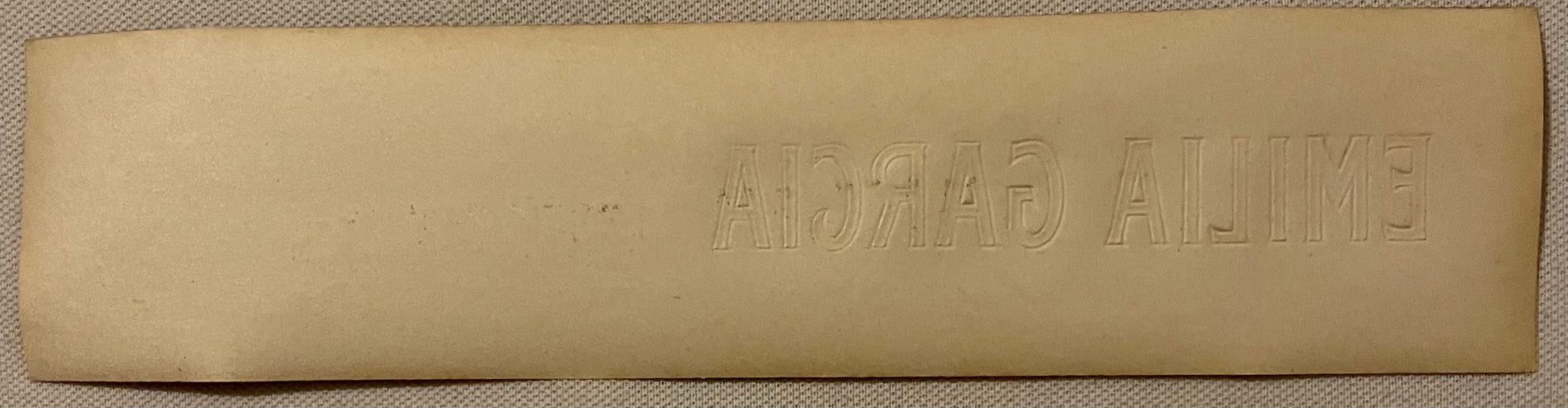Embossed tan cigar box label with "EMILIA GARCIA" text visible, shown flat against textured fabric background