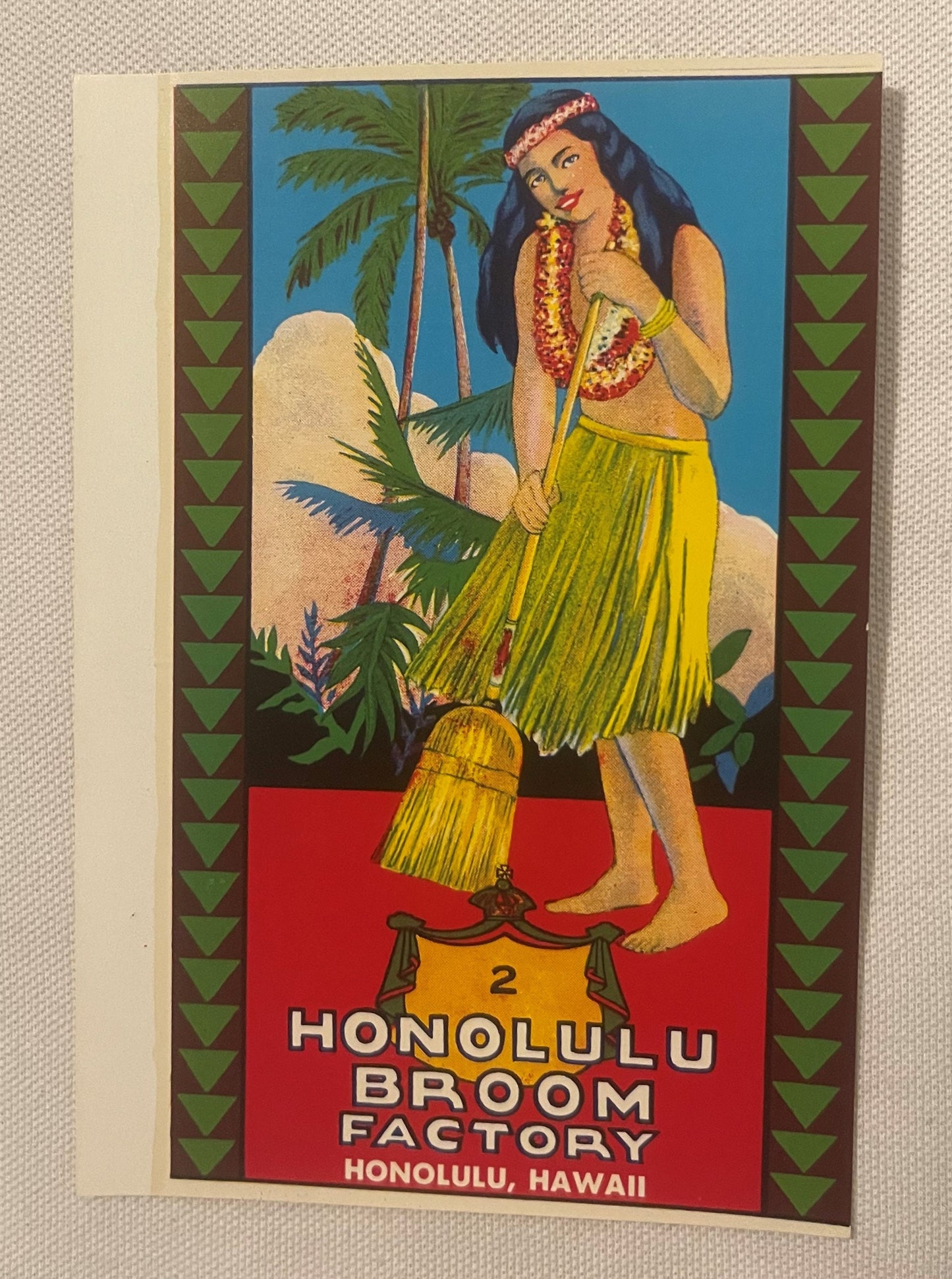 Vintage chromolithograph broom label featuring hula girl in yellow skirt with lei, palm trees, and decorative border on cream
