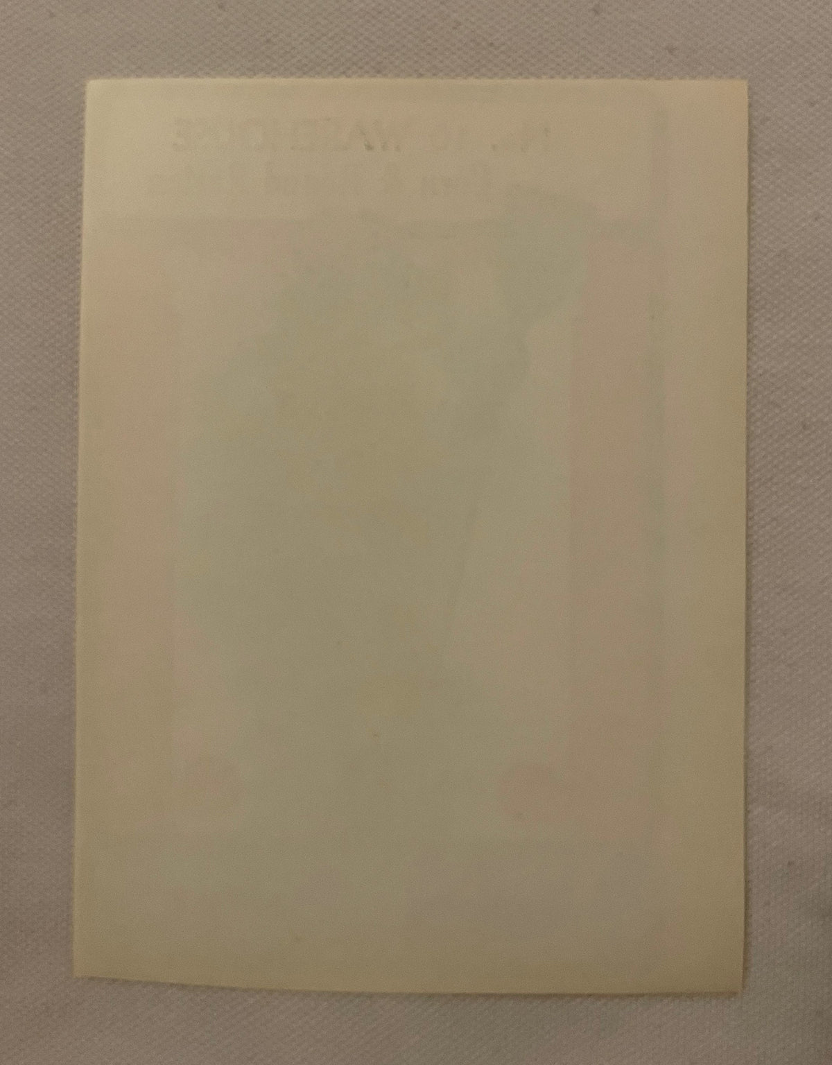 Cream-colored rectangular label or document on tan textile background, text barely visible due to age and lighting