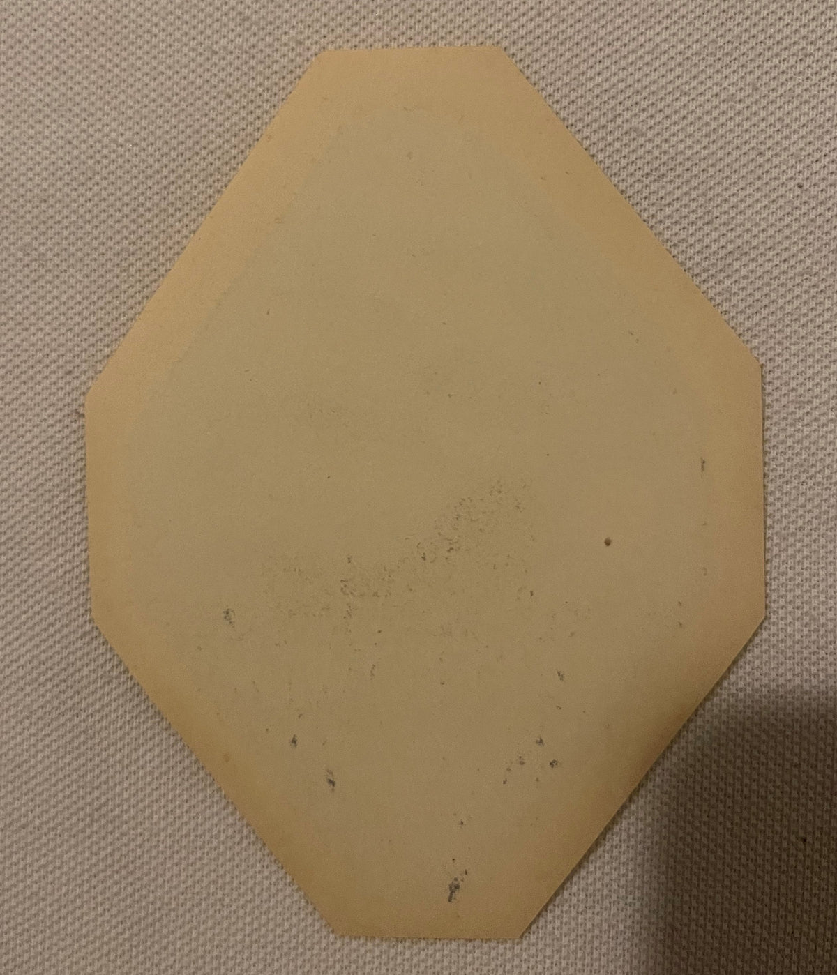 Tan hexagonal paper label with beveled corners on cream fabric background, showing age spots and discoloration
