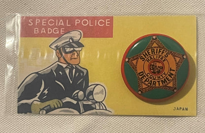 Vintage tin litho packaging for a sheriff's badge pin, showing illustrated policeman on motorcycle on left, brass star badge 