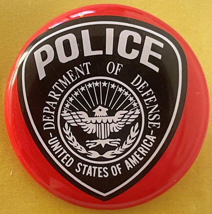 Circular red and black tin litho badge with white eagle seal and "POLICE - DEPARTMENT OF DEFENSE - UNITED STATES OF AMERICA" 