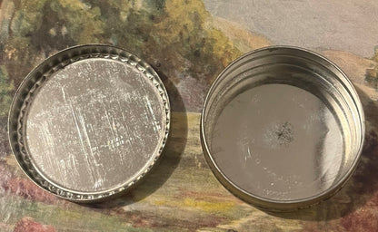 Two vintage metal tins shown from above on a mottled background; left tin has decorative crimped edges and embossed surface, 