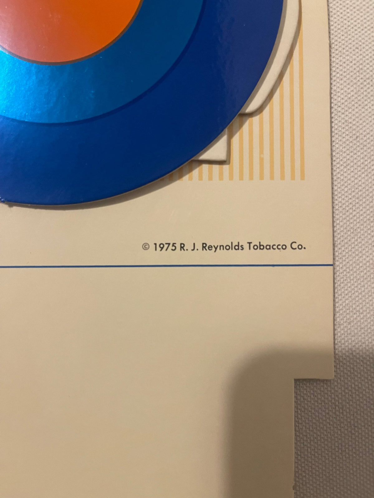 Close-up of vintage Vantage cigarette display sign showing blue curved design, orange circle, yellow stripes, and copyright t