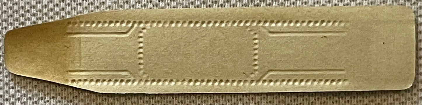 Gilt gold embossed cigar band with decorative dotted border and rectangular panels, shown flat against textured fabric backgr