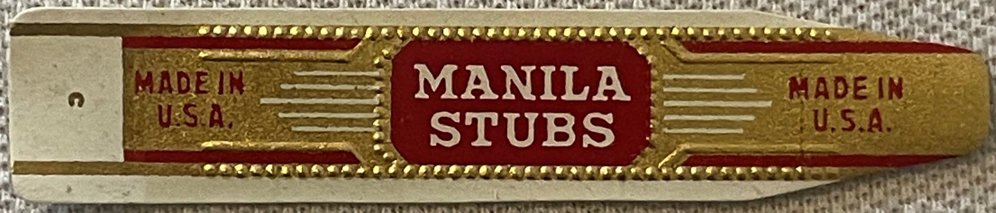 Vintage Manila Stubs cigar band label with gold and red embossed design, marked "Made in U.S.A." on both sides, against textu