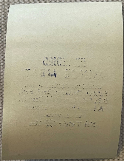 Aged cream-colored label with faded typewritten text, photographed flat against gray textured fabric background