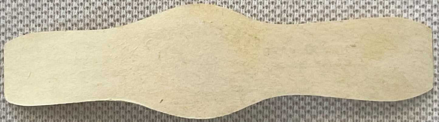 Cream-colored scalloped cigar band with wavy edges on textured gray fabric background