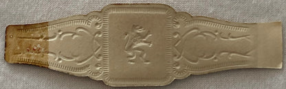 Ornate embossed cigar band with central profile portrait flanked by decorative scrollwork and shell motifs, tan metallic fini