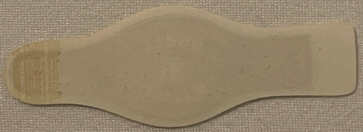 Cream-colored vintage cigar band with wavy edges laid flat on beige fabric, showing faint printed text on left side.