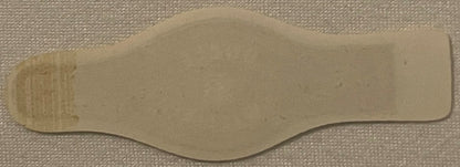 Cream-colored vintage cigar band with wavy edges laid flat on beige fabric, showing faint printed text on left side.