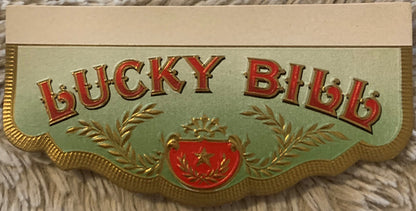 Gold-embossed vintage cigar box label with red "Lucky Bill" text, green background, laurel wreath design, and red shield embl