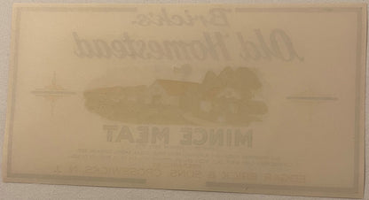 Back of the Brick's Old Homestead Mince Meat label: blank cream paper with no printing at all, showing only the front's farm scene and lettering ghosting through the sheet in mirror image