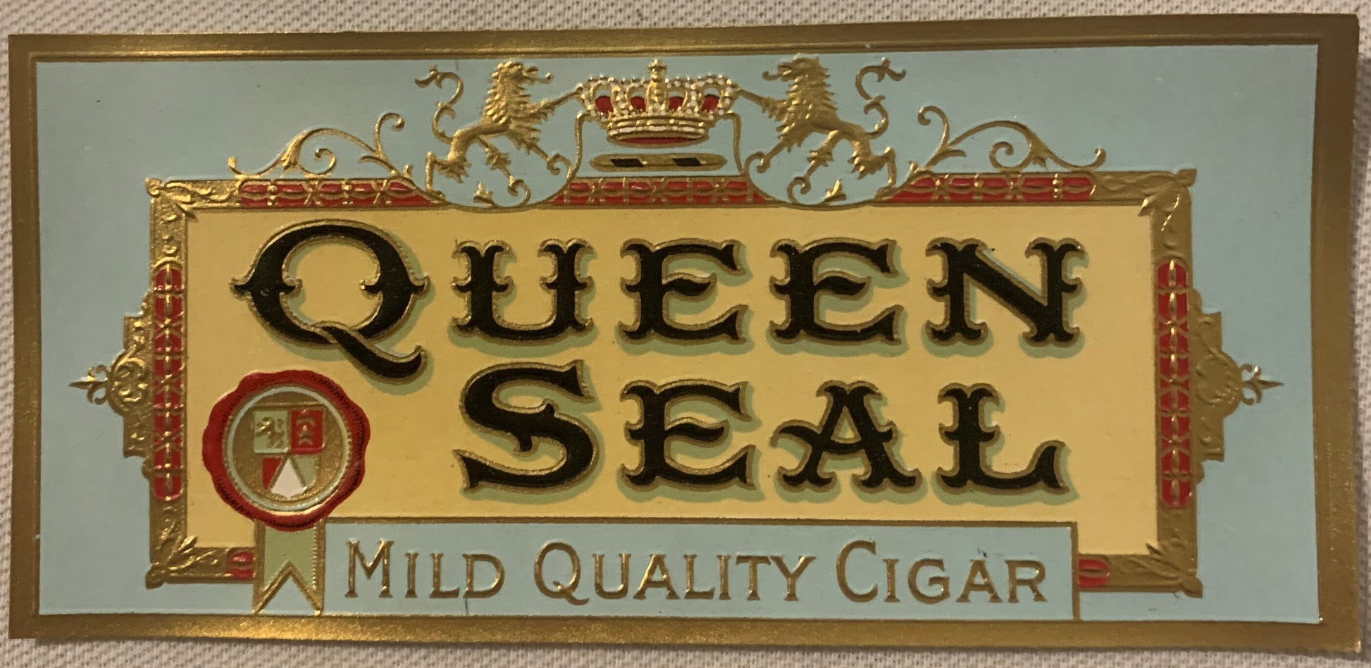 Gold embossed cigar box label reading "Queen Seal" with royal crown, shield, and decorative border on cream background, label
