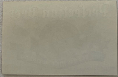 Blank cream-colored paper or label backing photographed flat against gray fabric surface