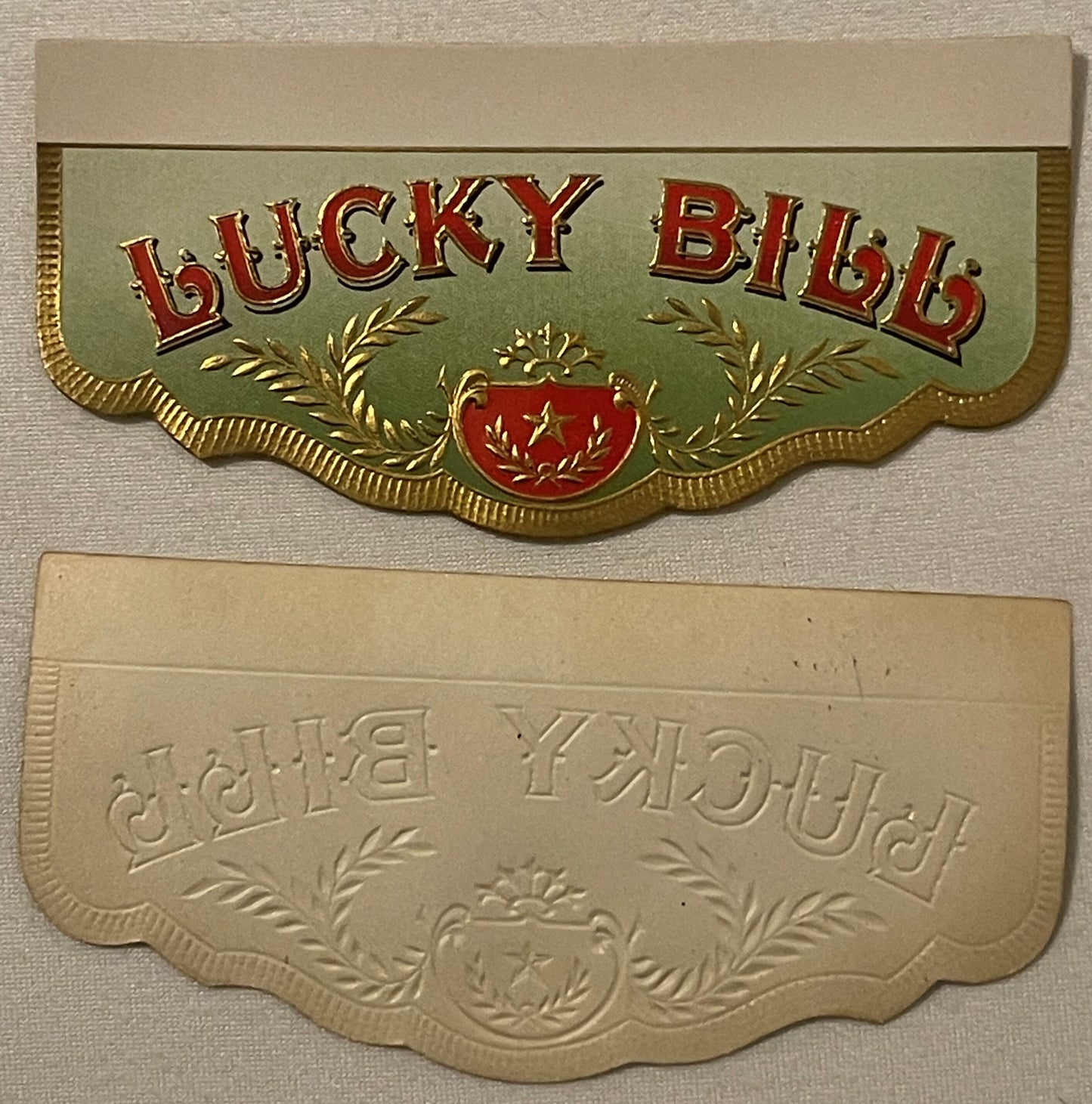 Two decorative cigar box label flaps with embossed gold borders and ornamental designs; top label shows "LUCKY BILL" in red a