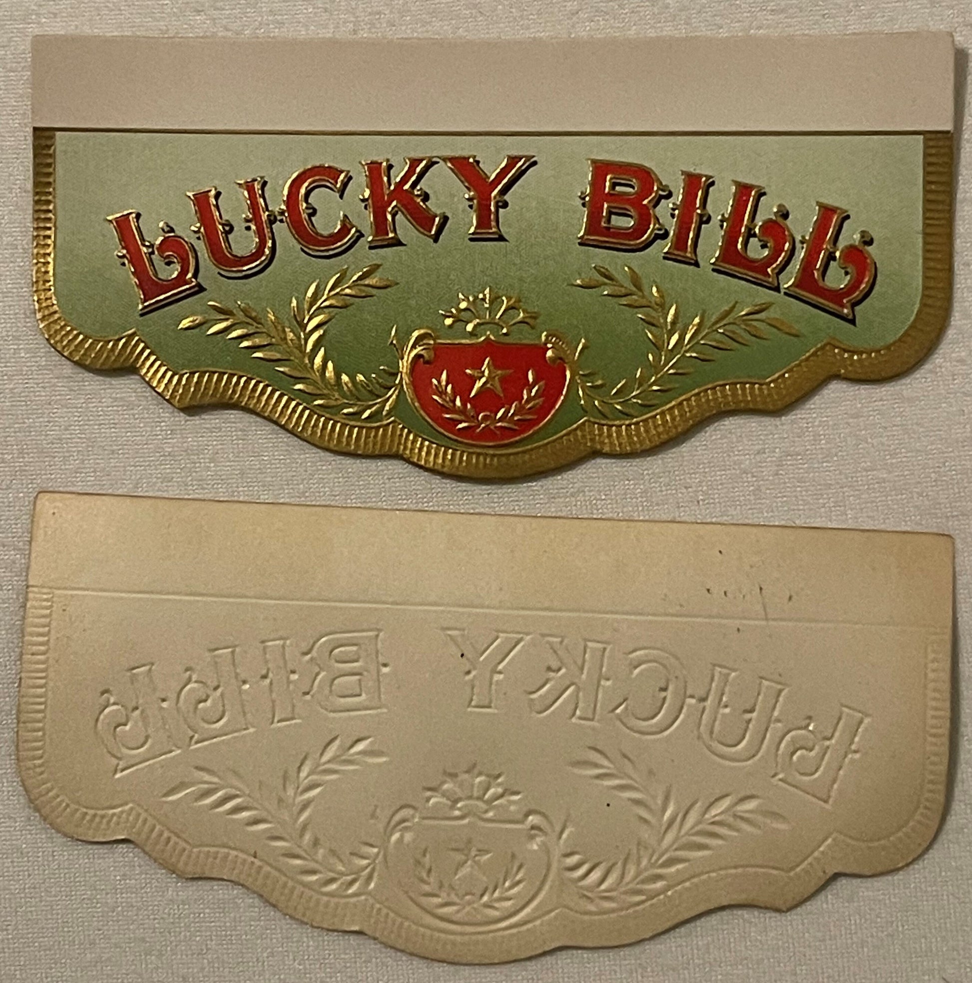 Two decorative cigar box label flaps with embossed gold borders and ornamental designs; top label shows "LUCKY BILL" in red a