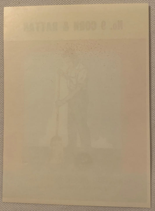 Back of the No. 9 Corn & Rattan broom label, plain cream paper with the mirrored front design faintly showing through, on a textured gray background.