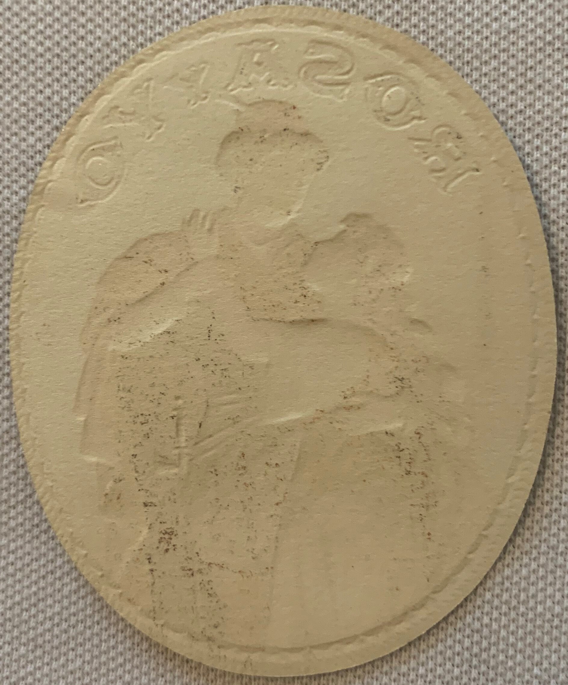 Cream-colored embossed oval cigar label with romantic couple portrait and ornate text border on beige fabric background